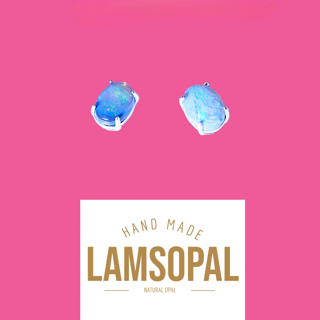 Two oval blue opal gemstone stud earrings in silver settings, shown above a white label with the text 'HAND MADE LAMSOPAL NATURAL OPAL' on a solid pink background.