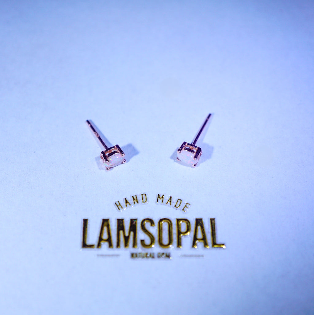 A pair of small stud earrings with clear square-cut stones in rose gold-toned settings, displayed on a light blue background above the brand name LAMSOPAL.