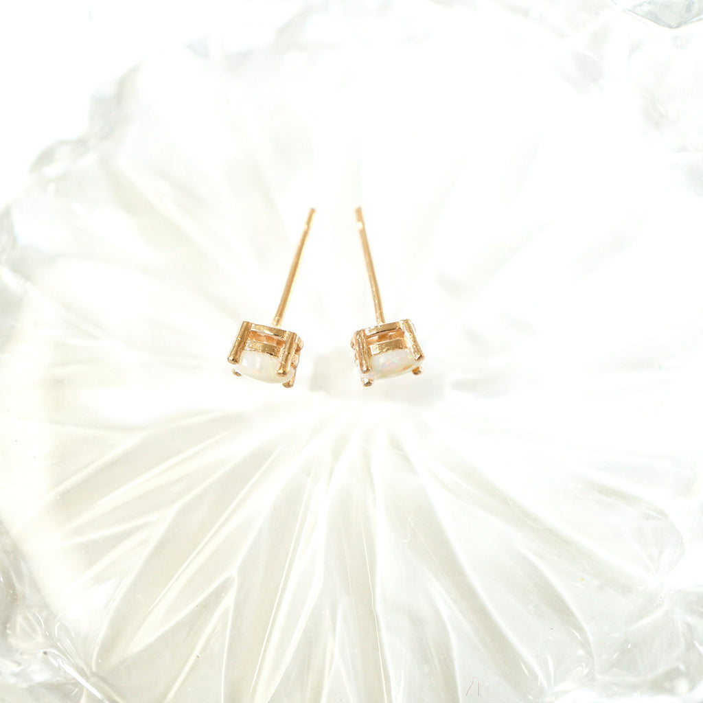 A pair of gold stud earrings with square-cut clear gemstones, displayed on a textured white surface.
