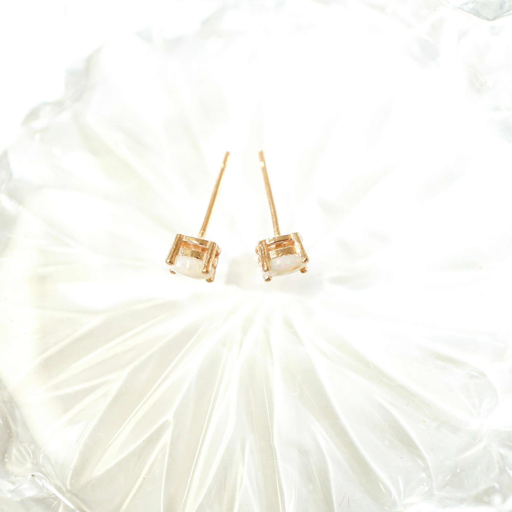 A pair of gold stud earrings with square-cut clear gemstones, displayed on a textured white surface.