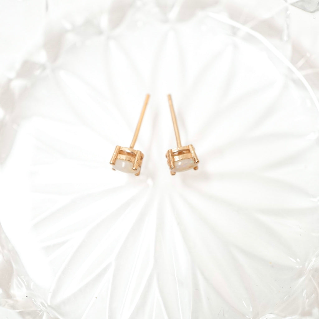A pair of gold stud earrings with small clear rectangular gemstones, displayed on a white textured glass plate.