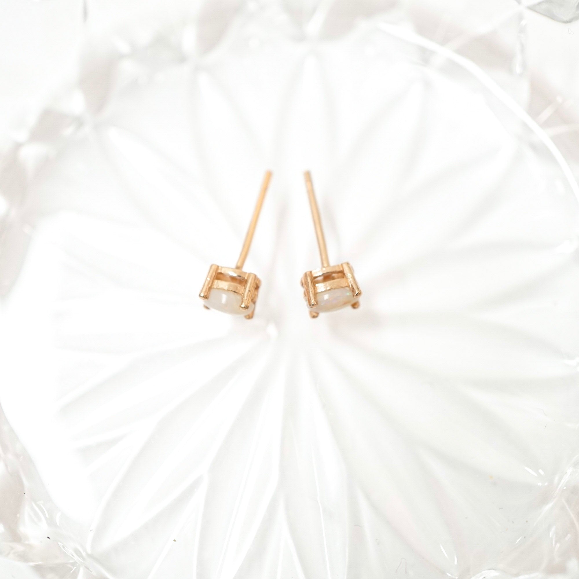 A pair of gold stud earrings with small clear rectangular gemstones, displayed on a white textured glass plate.