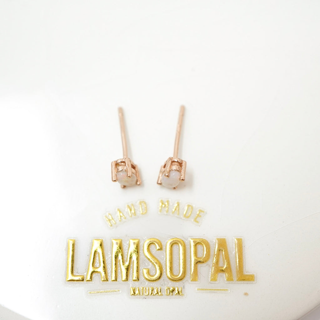 A pair of rose gold stud earrings with small square settings and pale white stones, displayed on a white background above gold foil branding that reads 'HAND MADE LAMSOPAL'.