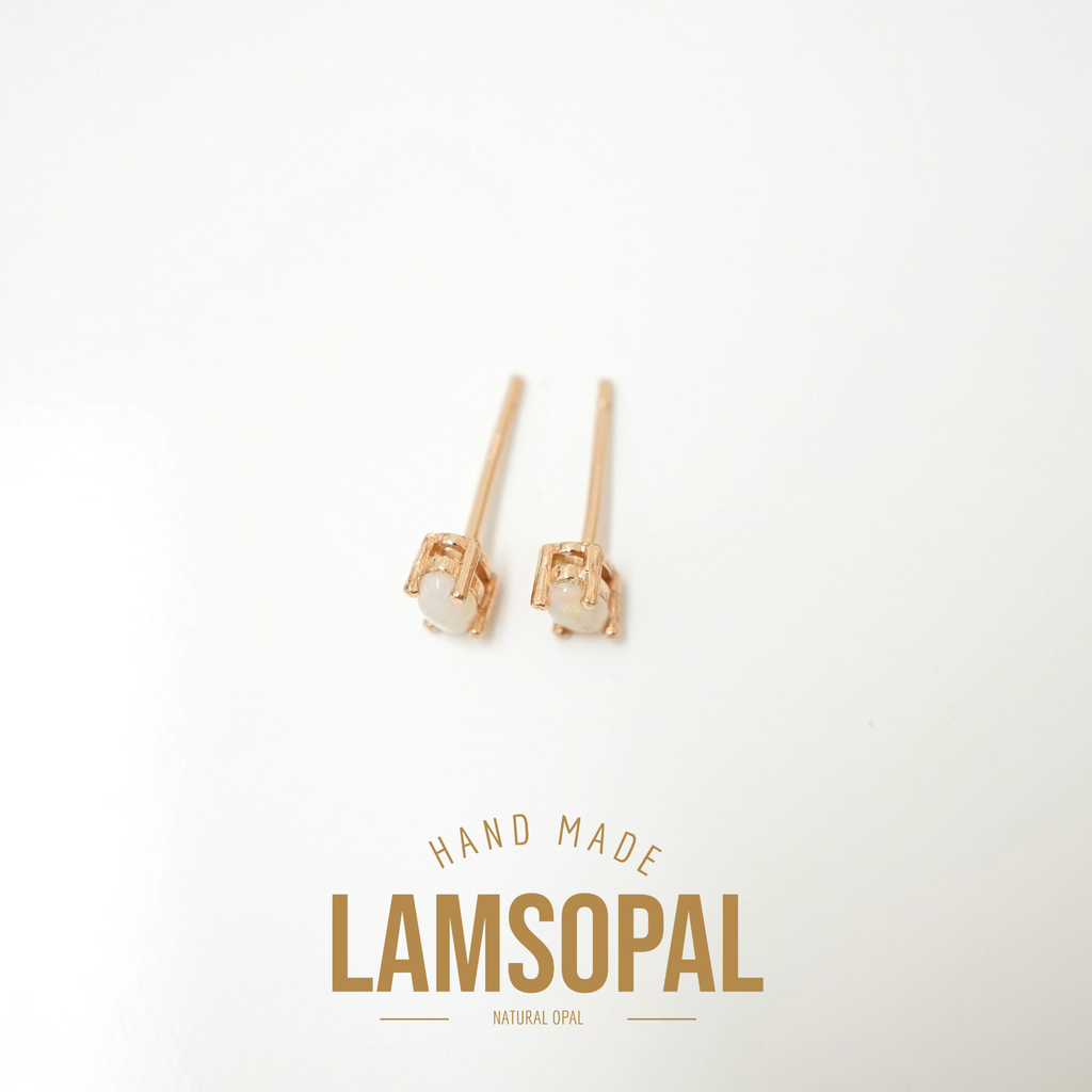 A pair of small rose gold stud earrings with oval white gemstones, displayed on a clean white background with a gold 'LAMSOPAL' brand logo and 'HAND MADE' text below.
