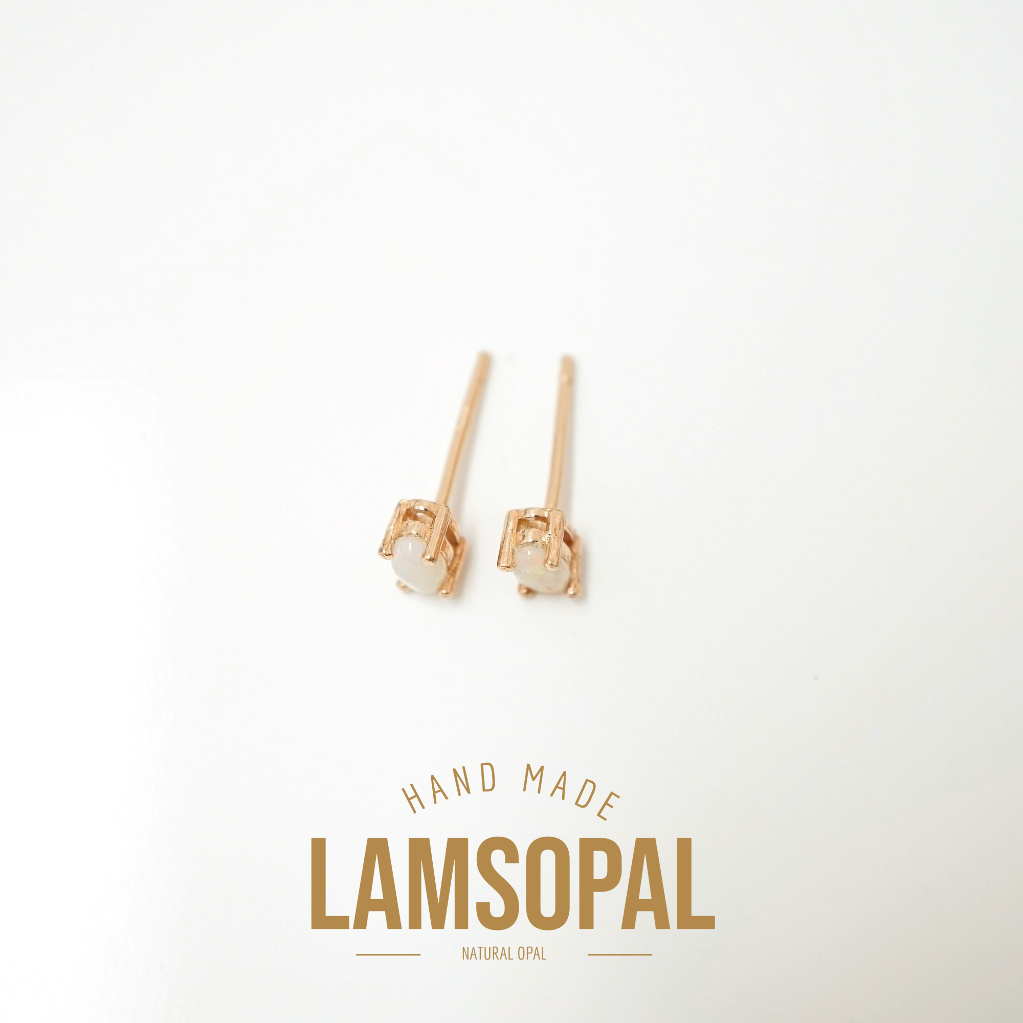 A pair of small rose gold stud earrings with oval white gemstones, displayed on a clean white background with a gold 'LAMSOPAL' brand logo and 'HAND MADE' text below.