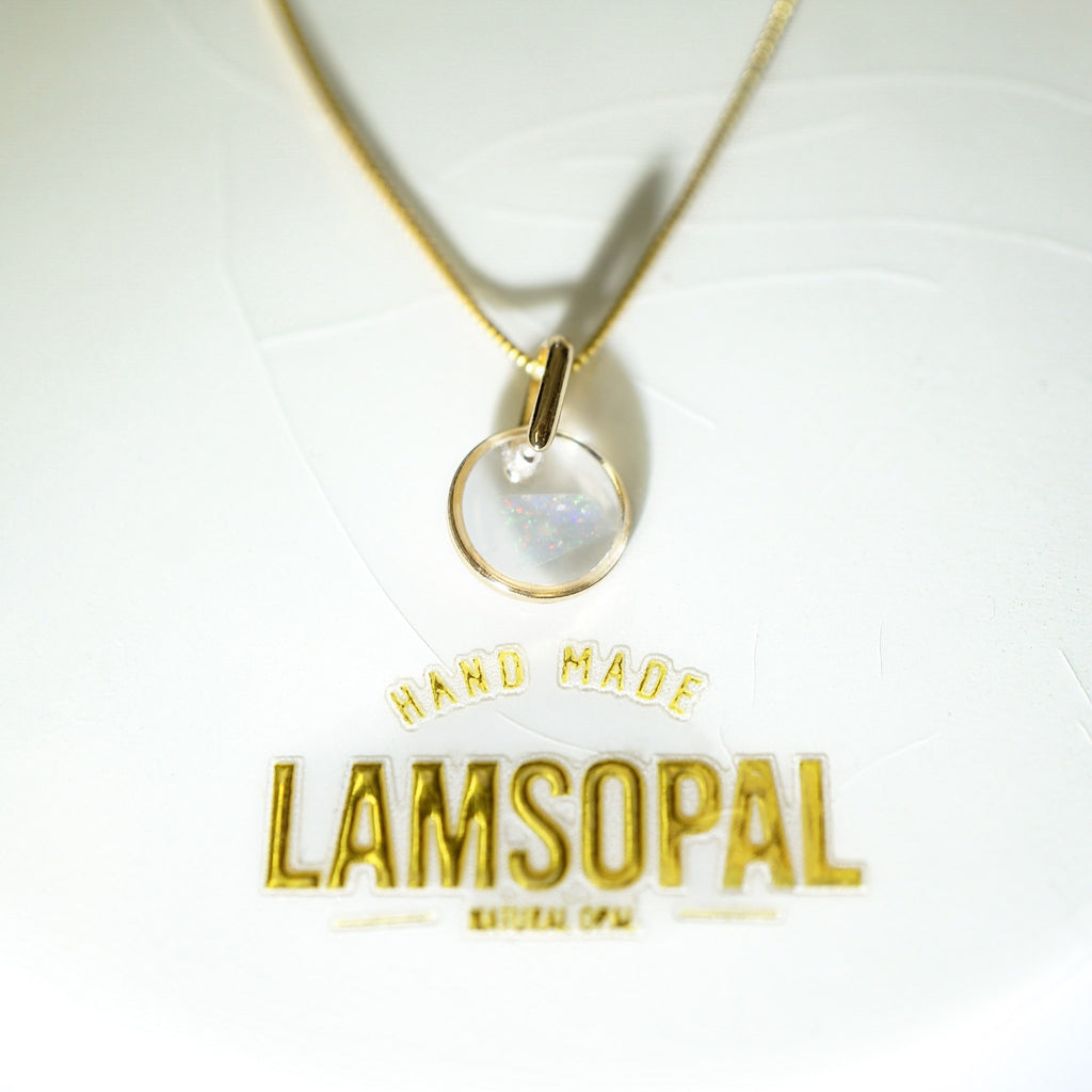A gold chain necklace with a circular pendant containing an iridescent moonstone, displayed on a white textured background with a gold 'LAMSOPAL' brand logo below.