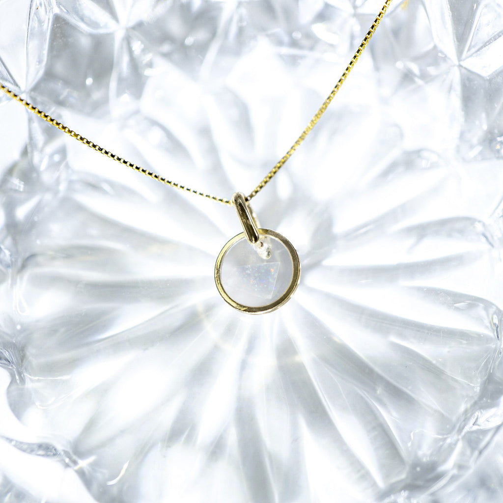 A delicate gold chain necklace with a minimalist, thin circular ring pendant, displayed on a textured, faceted clear glass plate.