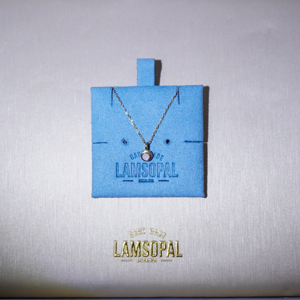 A delicate silver chain necklace with a small round pendant displayed on a bright blue Lamsopal jewelry card, set against a textured light gray background with the gold Lamsopal logo below.