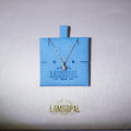 A delicate silver chain necklace with a small round pendant displayed on a bright blue Lamsopal jewelry card, set against a textured light gray background with the gold Lamsopal logo below.