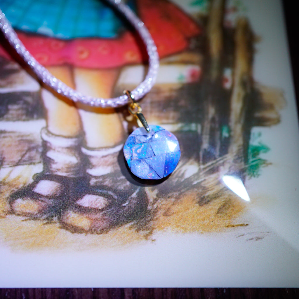 A close-up of a necklace with a faceted blue and white marbled pendant on a sparkly silver chain, resting on a painted illustration of a child's legs.