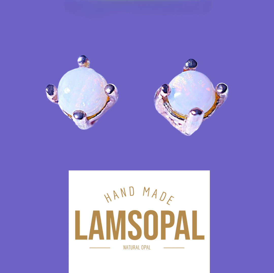 A pair of handmade Lamsopal natural opal stud earrings with silver settings and small dark accent stones, shown above a white label that reads 'HAND MADE LAMSOPAL NATURAL OPAL' on a solid purple background.
