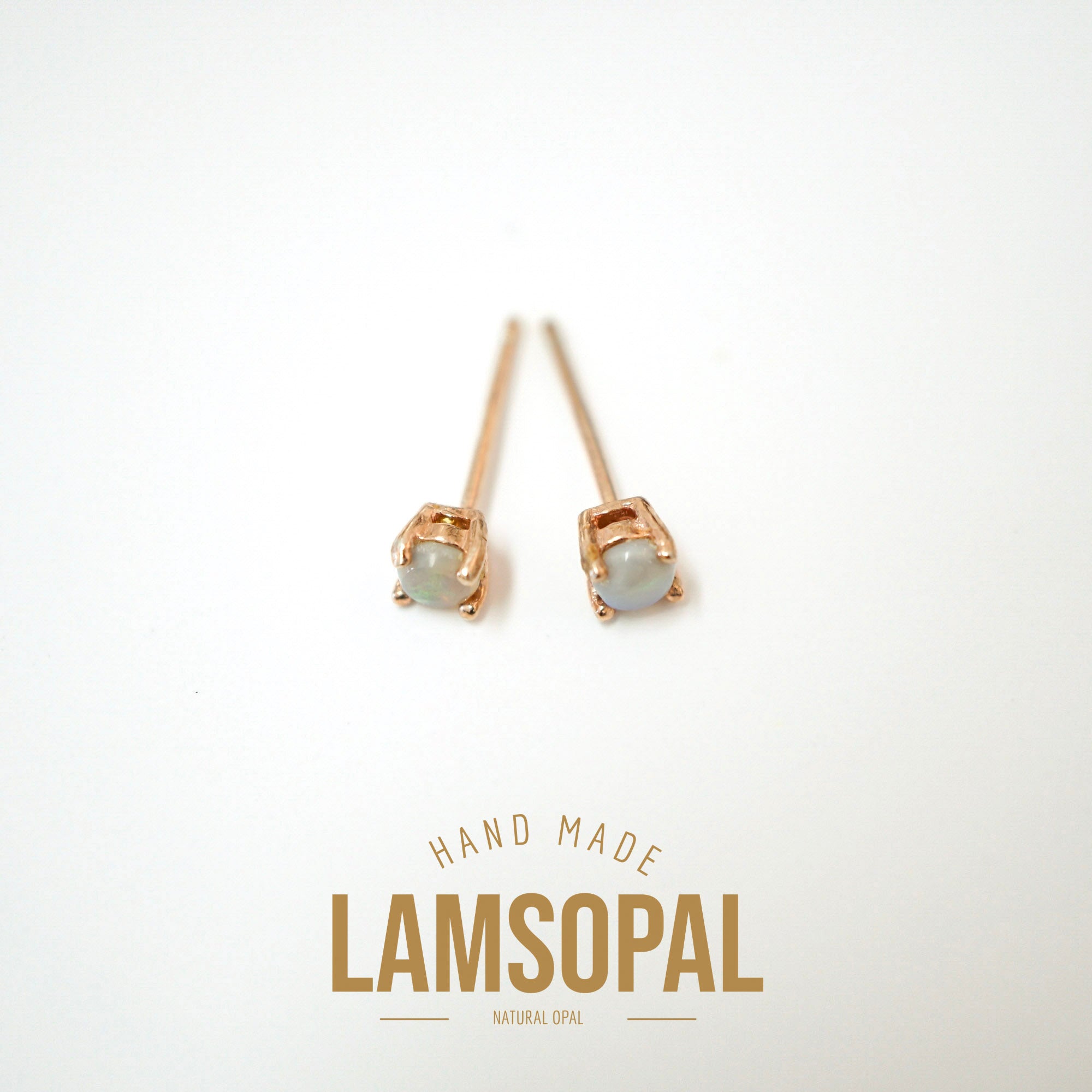 A pair of handmade Lamsopal stud earrings featuring natural opal gemstones in rose gold settings, displayed on a clean white background with a gold 'HAND MADE LAMSOPAL' text overlay at the bottom.