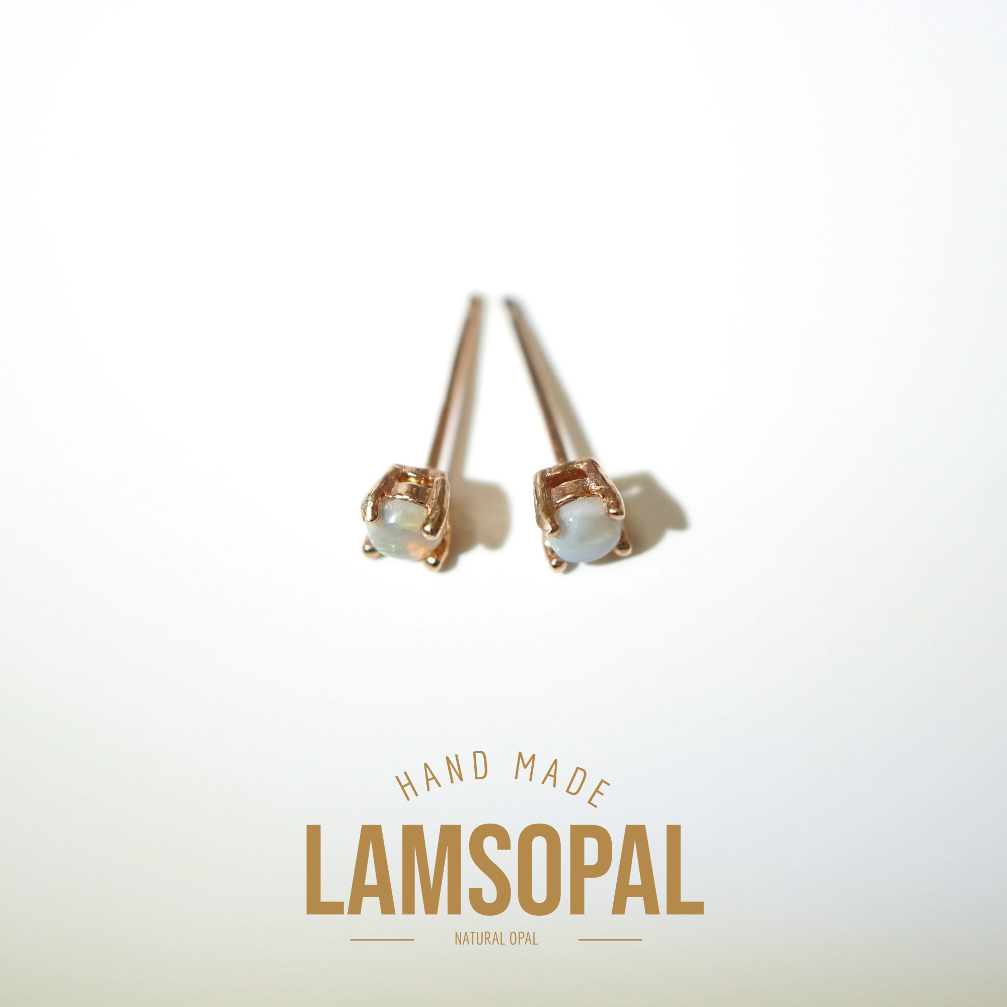 A pair of handmade Lamsopal stud earrings with natural opal stones in a rose gold setting, displayed on a clean white background with a gold-colored brand logo overlay at the bottom.