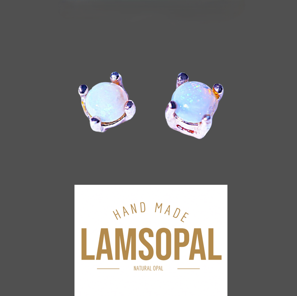 A pair of handmade Lamsopal natural opal stud earrings with a silver-toned setting and small dark accent stones, shown above a white label that reads 'HAND MADE LAMSOPAL NATURAL OPAL' on a dark gray background.