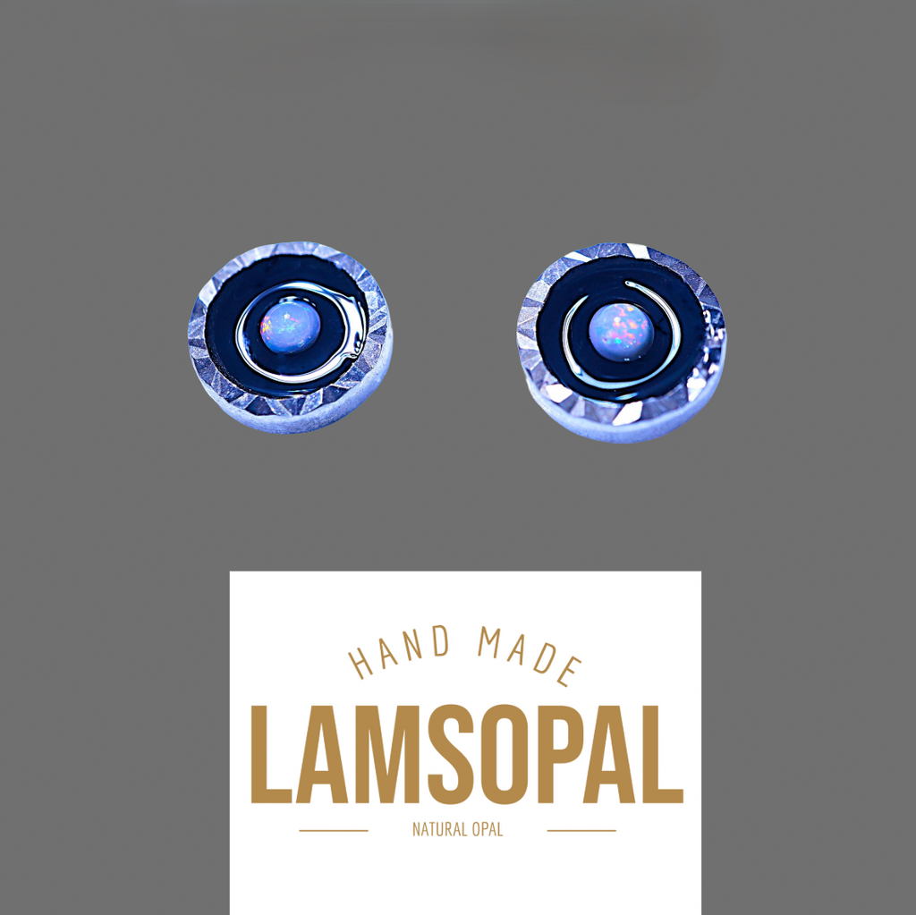 Two round handmade opal jewelry pieces with blue and silver inclusions, displayed above a white label that reads 'HAND MADE LAMSOPAL NATURAL OPAL' on a solid gray background.