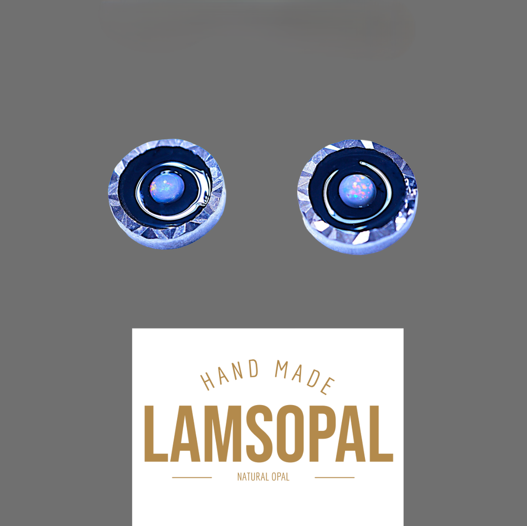 Two round handmade opal jewelry pieces with blue and silver inclusions, displayed above a white label that reads 'HAND MADE LAMSOPAL NATURAL OPAL' on a solid gray background.