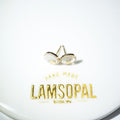 A pair of small gold stud earrings with oval white inlay, displayed on a white surface with the brand name 'LAMSOPAL' printed below.