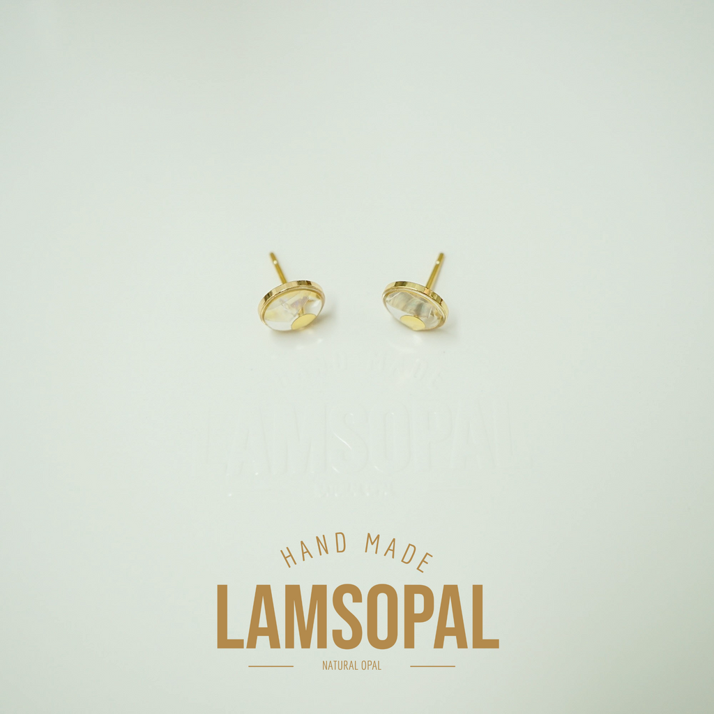 A pair of gold stud earrings with oval clear gemstones, displayed on a light cream background with a 'LAMSOPAL HAND MADE NATURAL OPAL' text overlay below.