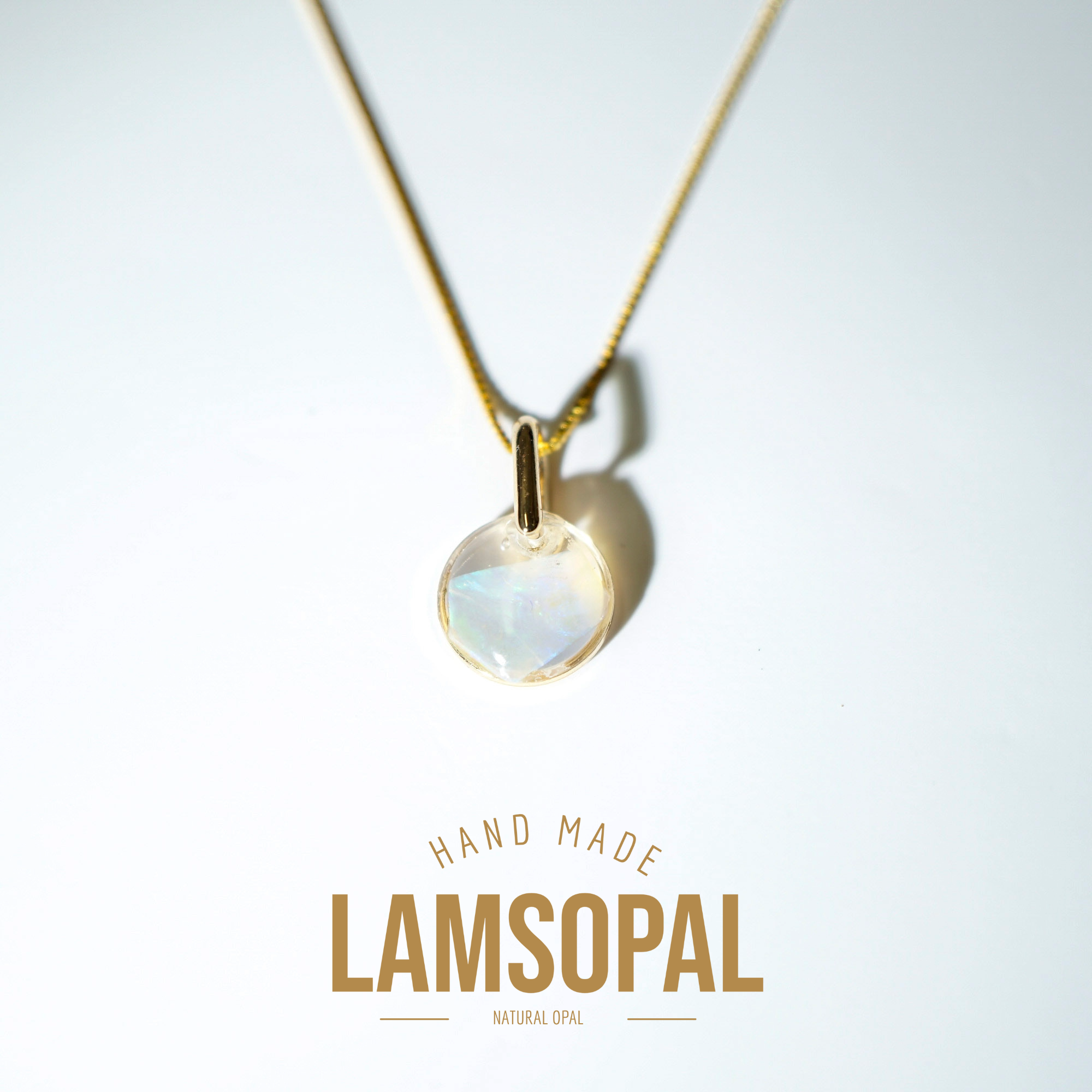 A gold chain necklace with a round iridescent Lamsopal pendant, displayed on a clean white background with a soft shadow. The text 'HAND MADE LAMSOPAL NATURAL OPAL' is printed below the pendant.