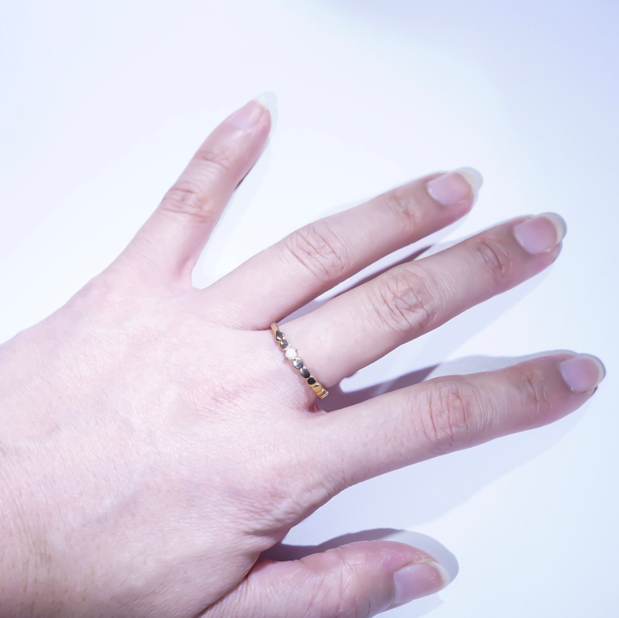 A close-up of a hand wearing a delicate gold ring with small clear stones on the ring finger, set against a plain white background.