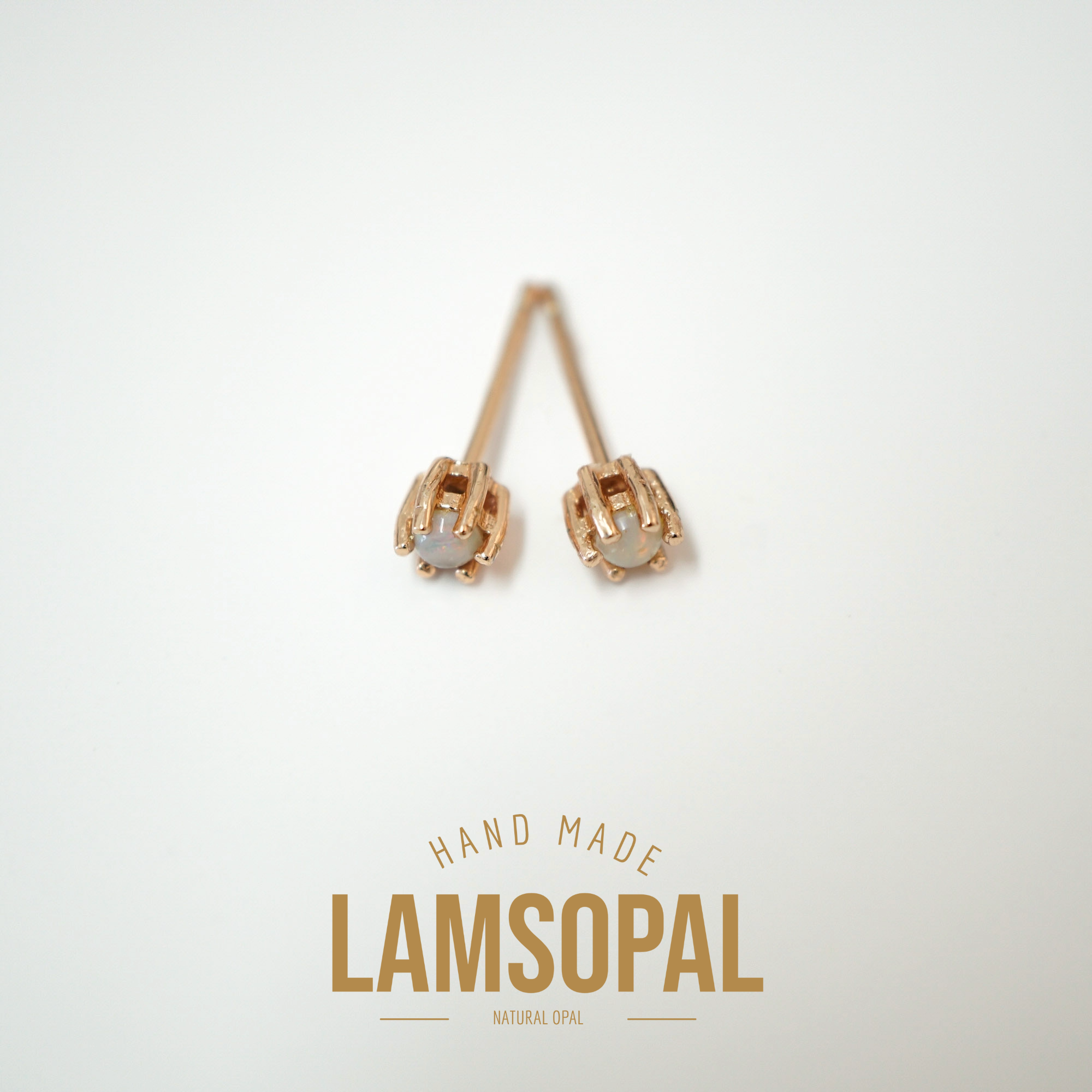 A pair of handmade rose gold stud earrings with oval gray-blue opal centers, displayed on a clean white background with 'HAND MADE LAMSOPAL NATURAL OPAL' text below.