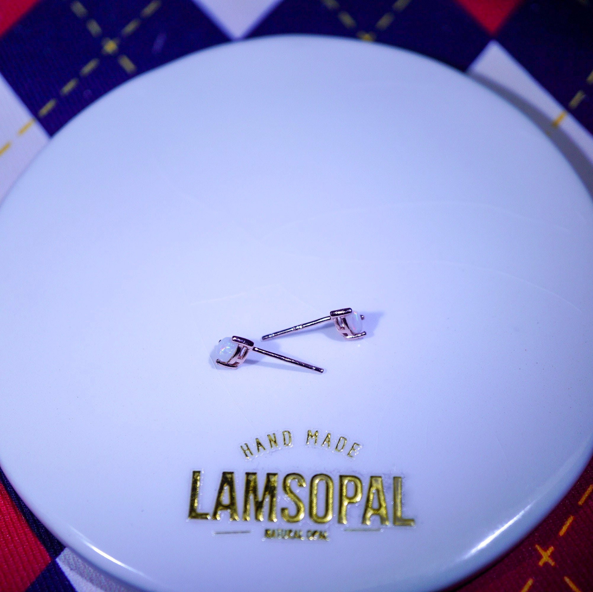 Earrings on a LAMSOPAL branded container with a checkered background