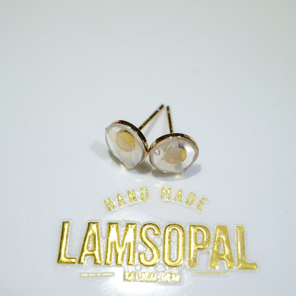 A pair of gold stud earrings with clear faceted round stones, displayed on a white surface above a gold 'LAMSOPAL HAND MADE' sticker.
