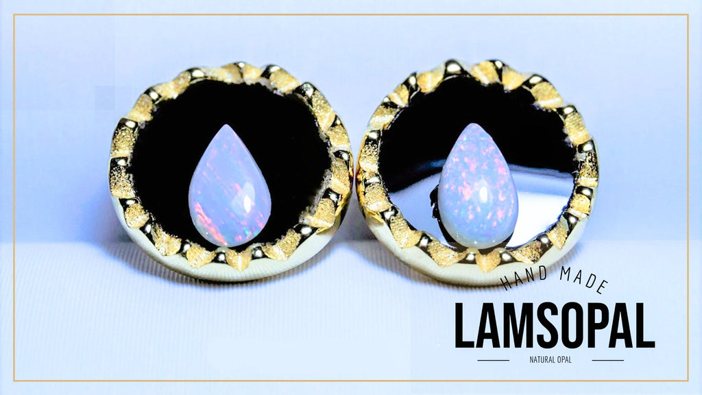 A pair of handmade Lamsopal natural opal earrings with teardrop-shaped iridescent opal centers set in gold and black bezel settings, displayed on a light blue background with a brand logo overlay.