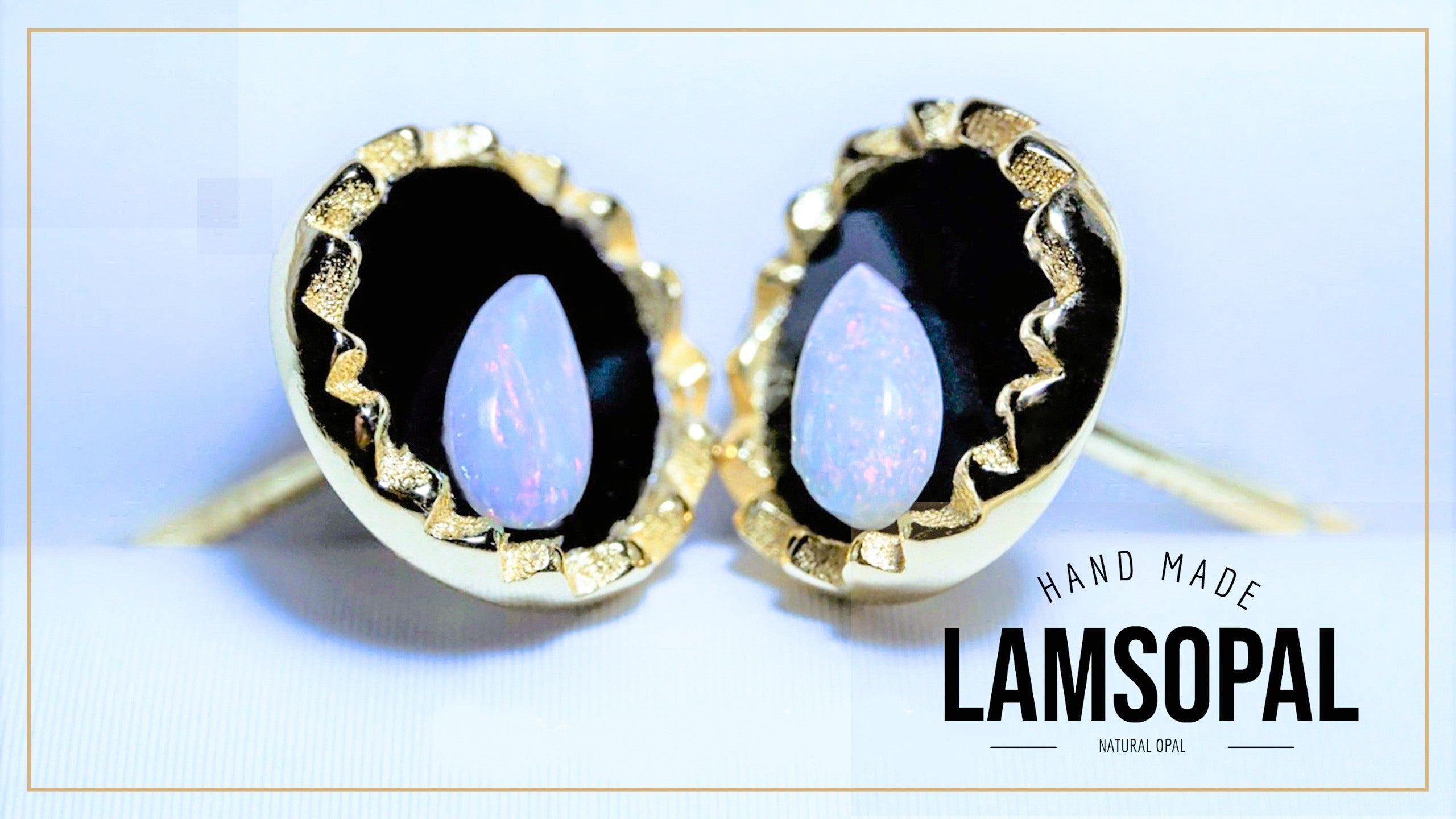 A pair of handmade Lamsopal stud earrings featuring natural opal stones with a blue iridescent sheen, set in gold bezel settings with a black background and textured gold borders. The image includes a text overlay on the bottom right reading 'HAND MADE LAMSOPAL NATURAL OPAL'.