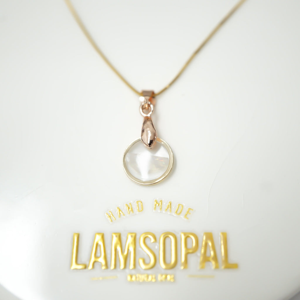 A delicate gold chain necklace with a small teardrop-shaped rose gold pendant holding a round, milky white stone, displayed on a white background with gold 'LAMSOPAL HAND MADE' branding below.