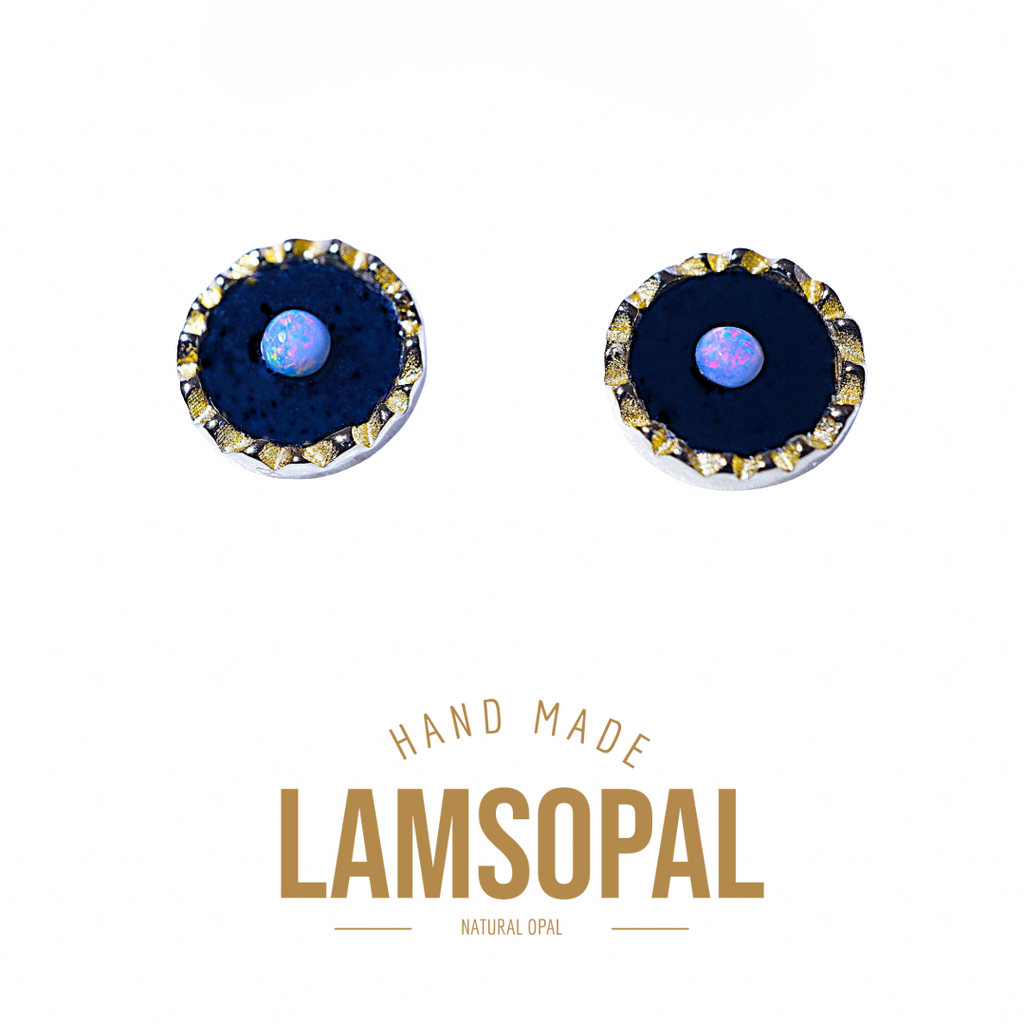 A pair of Lamsopal natural opal stud earrings with a deep blue bezel setting and a textured gold-toned scalloped rim, featuring a central iridescent blue-white opal. The brand name 'LAMSOPAL' is displayed below the earrings on a clean white background.