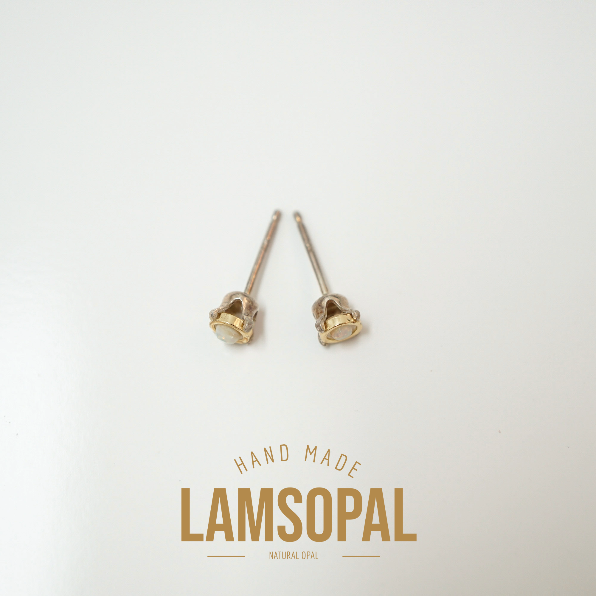 A pair of small gold stud earrings with oval cream-colored stones, displayed on a clean white background with a 'LAMSOPAL' brand logo at the bottom.