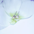 A pair of silver stud earrings with oval clear stones, resting on the delicate petals of a white flower.
