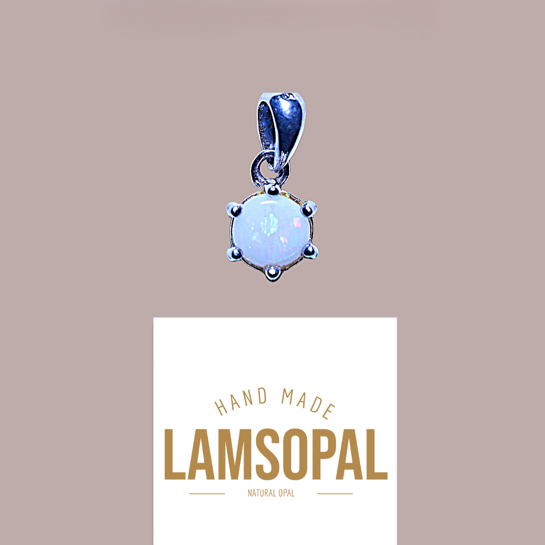 A sterling silver pendant featuring a round, milky white opal gemstone with subtle blue-green flashes, set in a prong setting. The pendant is shown above a white card displaying the brand name 'LAMSOPAL' and the text 'HAND MADE NATURAL OPAL' on a solid taupe background.