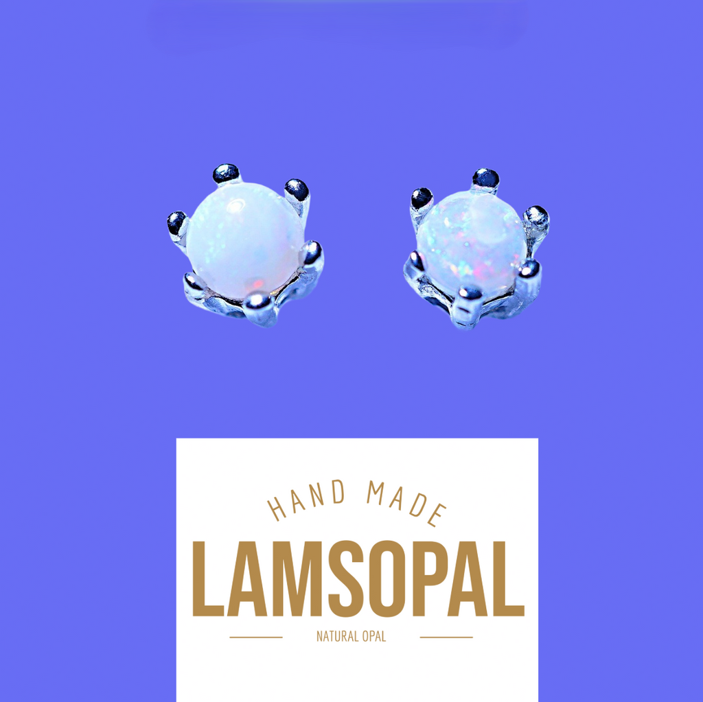 A pair of handmade crown-shaped opal stud earrings with silver settings and white iridescent opal centers, shown above a white label that reads 'HAND MADE LAMSOPAL NATURAL OPAL' on a solid purple background.