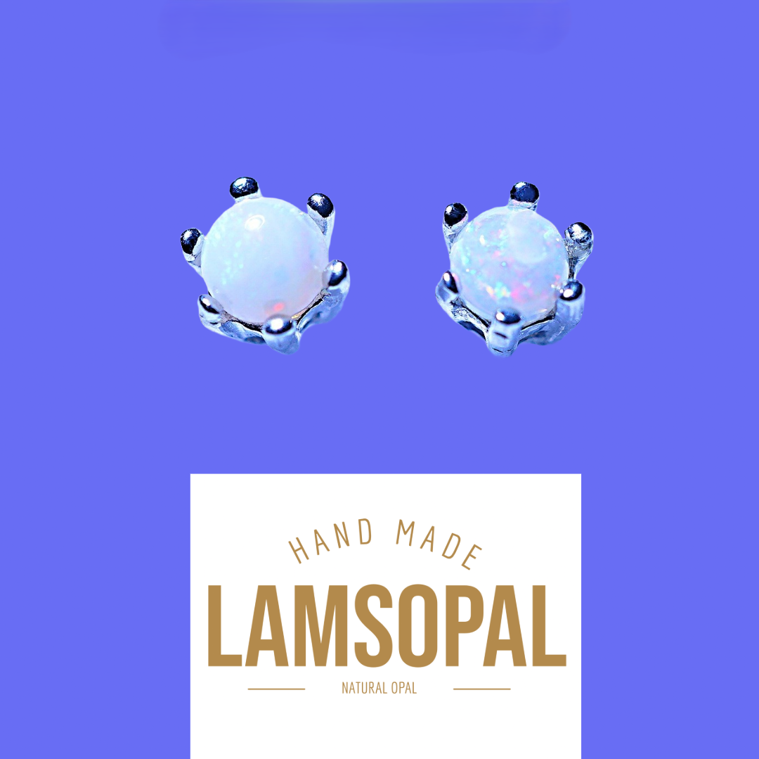 A pair of handmade crown-shaped opal stud earrings with silver settings and white iridescent opal centers, shown above a white label that reads 'HAND MADE LAMSOPAL NATURAL OPAL' on a solid purple background.