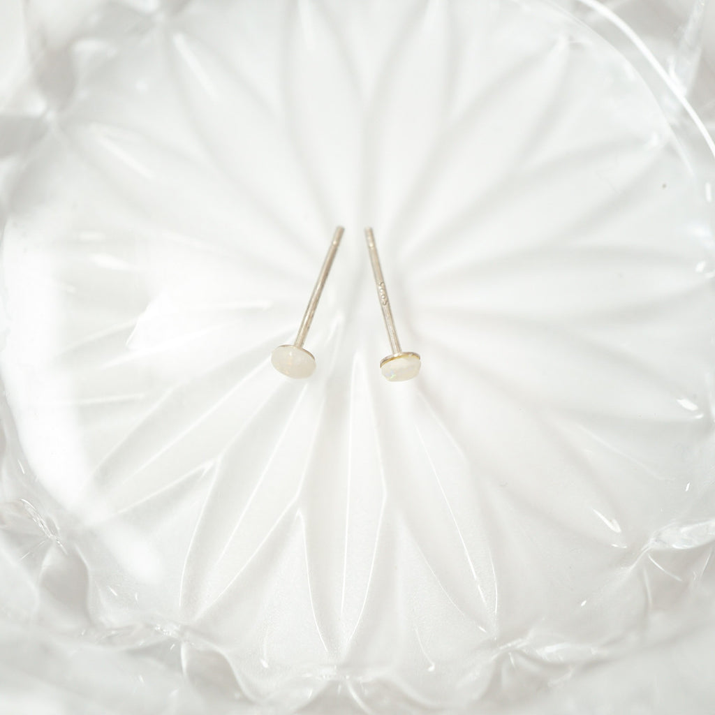 Two small gold post earrings with round dome-shaped gold tops, displayed on a textured white glass dish.