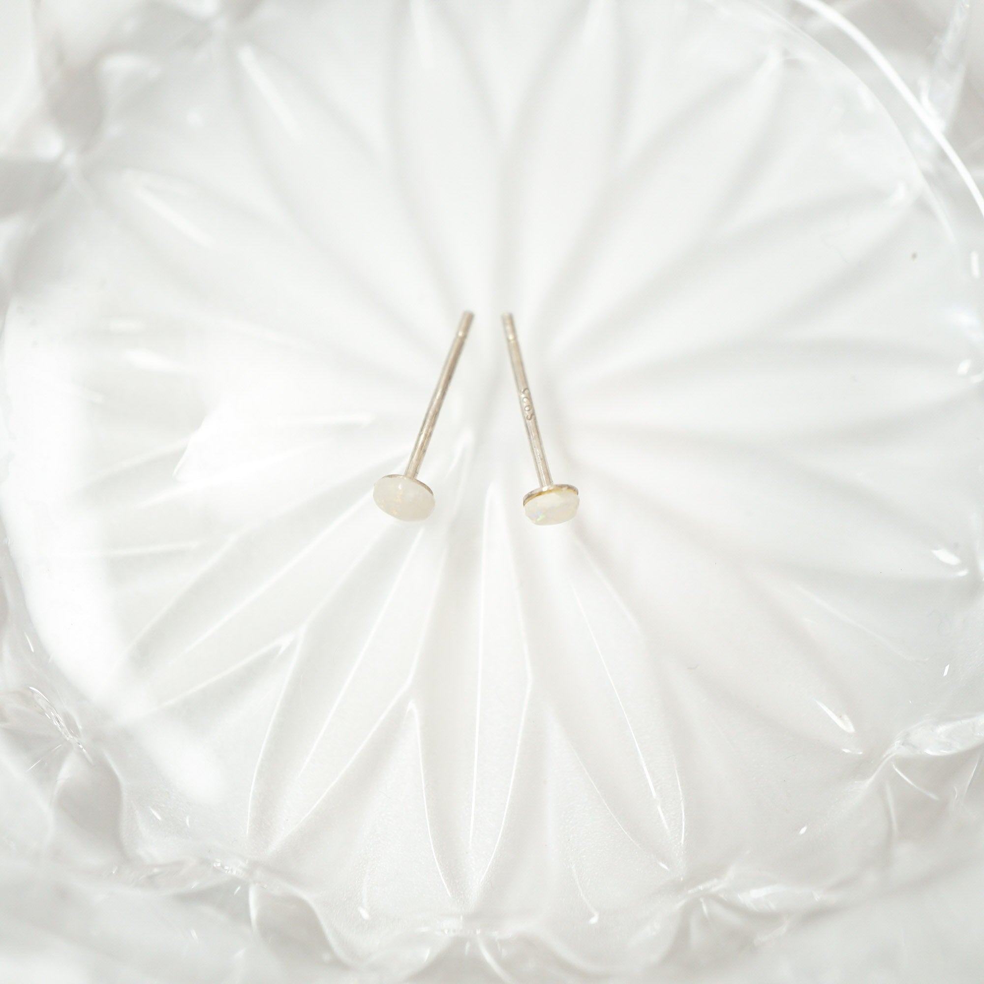 Two small gold post earrings with round dome-shaped gold tops, displayed on a textured white glass dish.