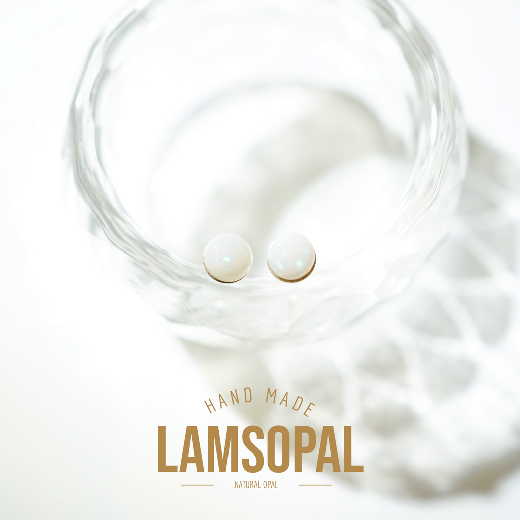 Two round natural opal gemstones displayed inside a clear glass bowl, with a gold text overlay reading 'HAND MADE LAMSOPAL NATURAL OPAL' on a bright white background.