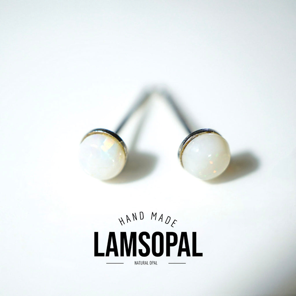 A pair of Lamsopal natural opal stud earrings with white iridescent cabochons and silver posts, displayed on a clean white background with a brand logo overlay.