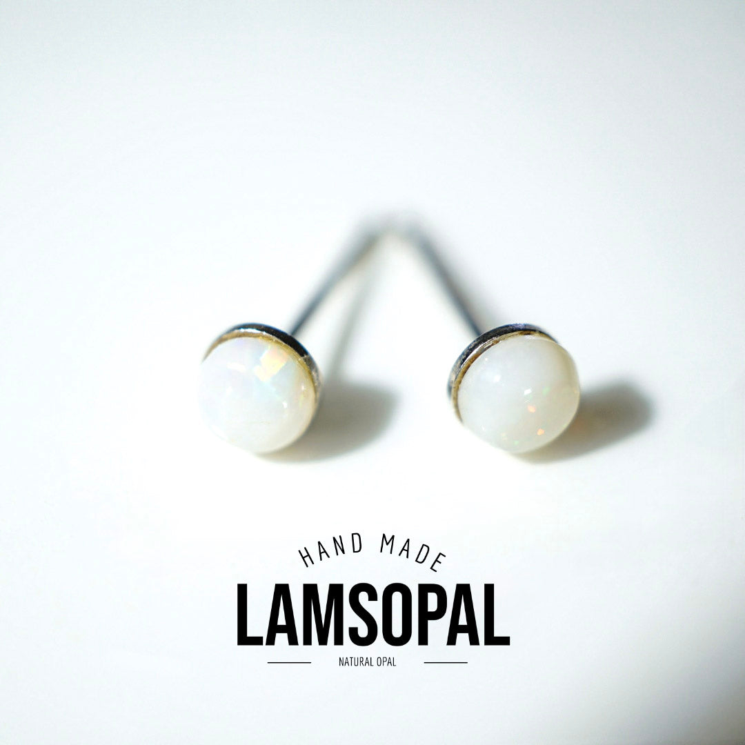 A pair of Lamsopal natural opal stud earrings with white iridescent cabochons and silver posts, displayed on a clean white background with a brand logo overlay.