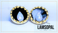 Two handmade Lamsopal natural opal teardrop stud earrings set in gold and white bezel settings, displayed side-by-side on a light blue background with a 'HAND MADE LAMSOPAL' text overlay.