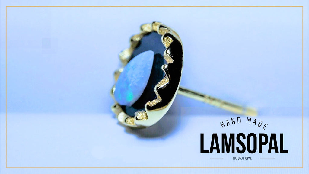 A gold-plated Lamsopal stud earring featuring a natural blue opal gemstone, set against a light blue background with a gold border and a text overlay reading 'HAND MADE LAMSOPAL'.