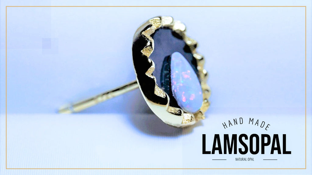 A single handmade Lamsopal stud earring featuring a natural opal with iridescent blue, purple, and green flashes, set in a gold bezel with a black enamel border. The earring is shown on a light blue background with a gold border, and the text 'HAND MADE LAMSOPAL' is visible in the bottom right corner.