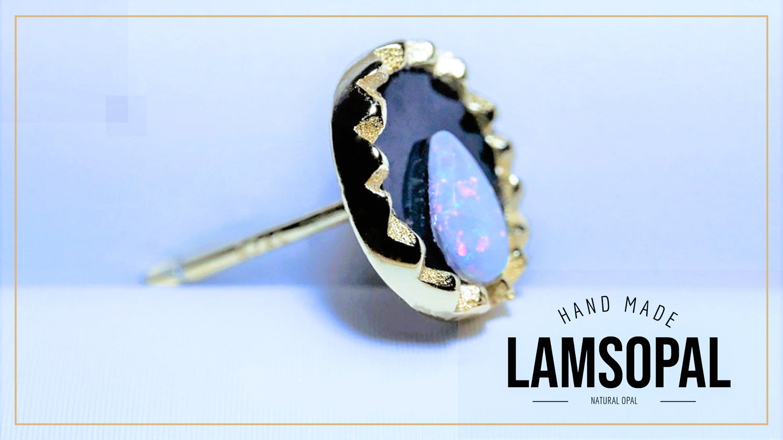 A single handmade Lamsopal stud earring featuring a natural opal with iridescent blue, purple, and green flashes, set in a gold bezel with a black enamel border. The earring is shown on a light blue background with a gold border, and the text 'HAND MADE LAMSOPAL' is visible in the bottom right corner.