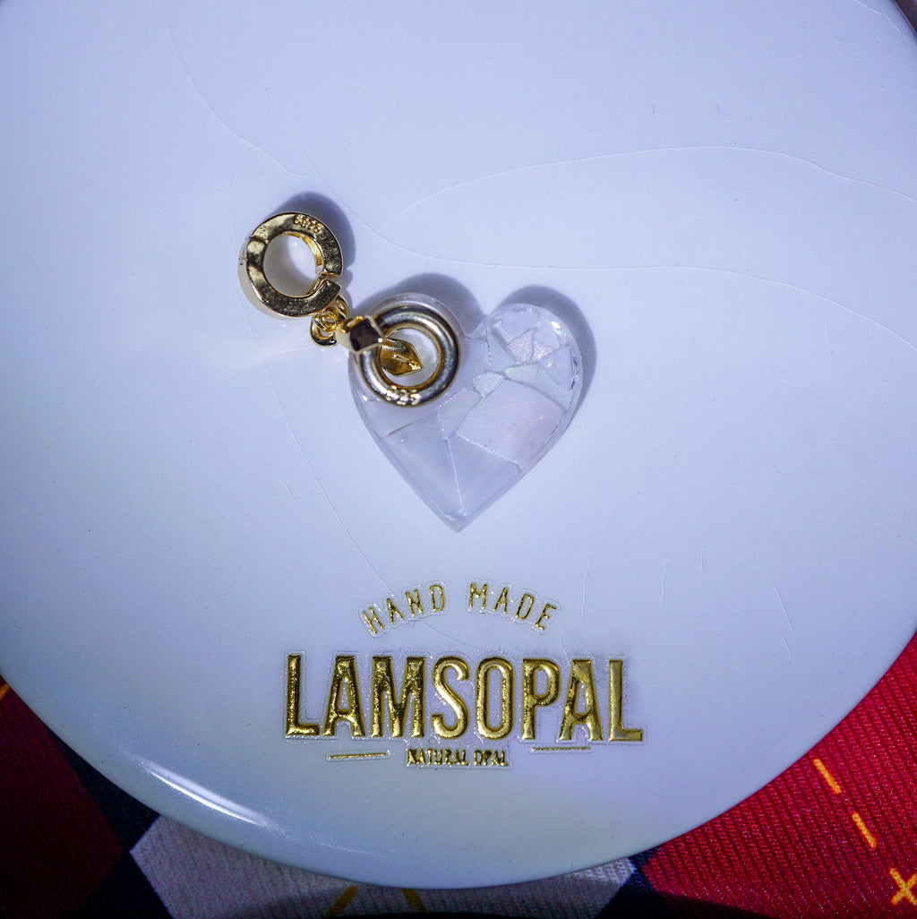 Close-up of a white opal pendant with 'LAMSOPAL' branding and a heart-shaped tag.